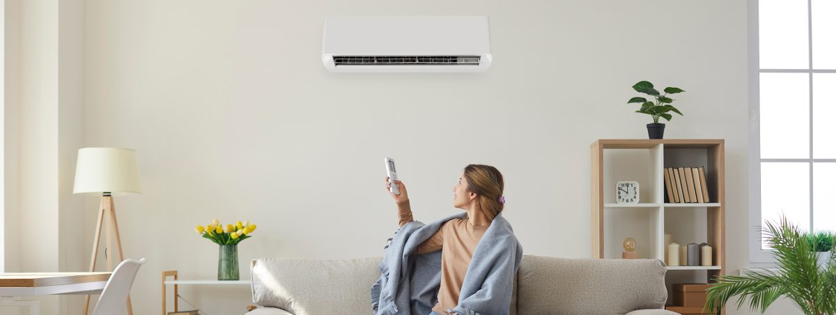 Woman enjoying cool fresh air in her living room with air conditioner on the wall